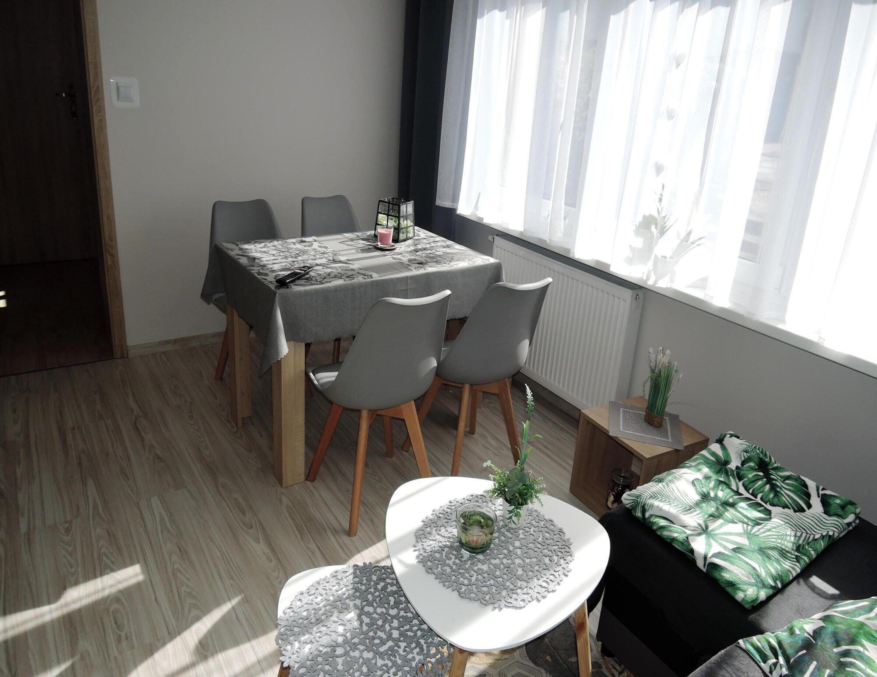 A modern dining area with a table set for two, a small side table with a plant, and a sofa with a tropical print cushion.