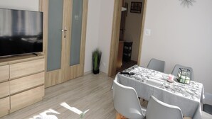 A modern living room with a flat-screen TV, wooden cabinets, a dining table with chairs, and a small plant. - Seaside Apartment in Dziwnow Baltic (Dziwnów)