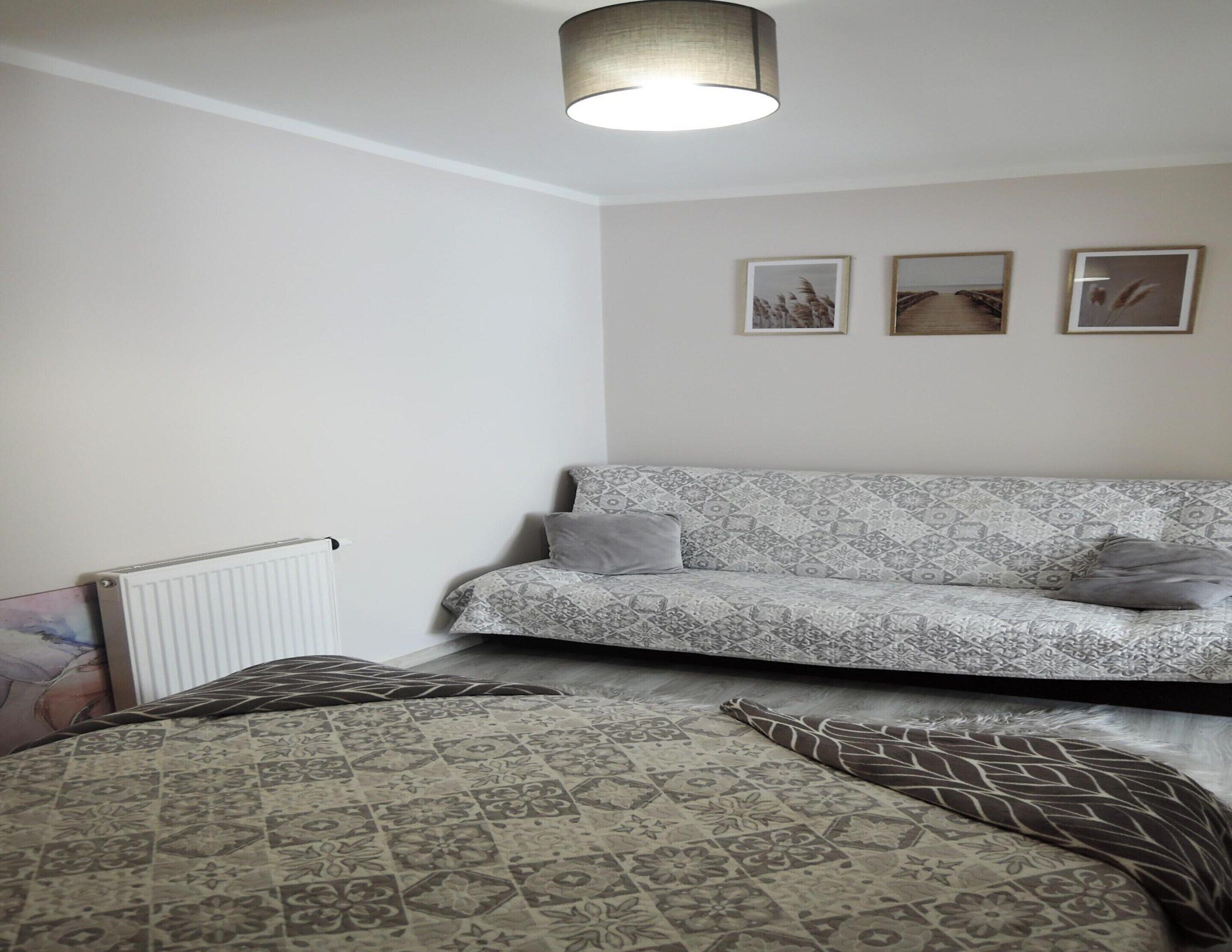 A bedroom with a patterned sofa, a bed with a patterned bedspread, a radiator, and three framed pictures on the wall.
