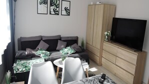 A modern living room with a sofa, a TV, a wooden cabinet, and a dining area with a table and chairs. - Seaside Apartment in Dziwnow Baltic (Dziwnów)