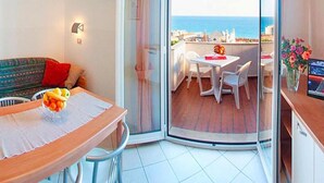 A room with a dining table and chairs, a sofa, and a view of the sea through a glass door. - Holiday Flat in Pretty Residence With Communal Pool in Pietra Ligure (Pietra Ligure)