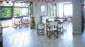 A spacious room with tiled flooring, wooden chairs, and tables. There are large windows allowing natural light, and the room is decorated with international flags. - Holiday Flat in Pretty Residence With Communal Pool in Pietra Ligure (Pietra Ligure)