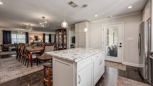 Una cocina amplia con una isla grande, armarios blancos e iluminación colgante moderna.