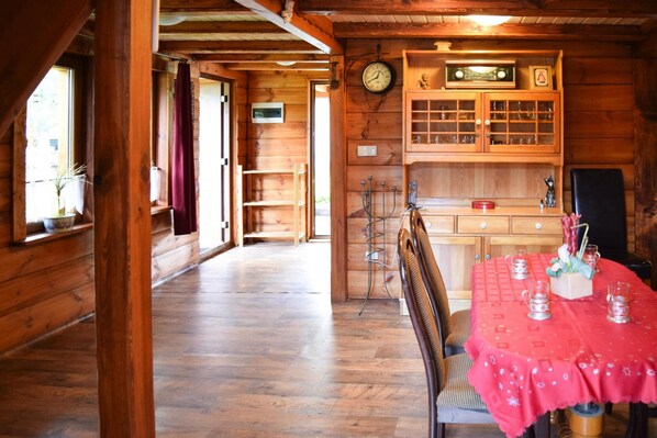 A wooden cabin interior with a dining table set for two, a clock on the wall, and a kitchen area with cabinets and a sink. - Cozy Holiday Home, Junoszyno (Stegna)