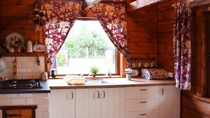 A rustic kitchen with wooden cabinets, a sink, and a window with floral curtains. - Cozy Holiday Home, Junoszyno (Stegna)