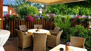 An outdoor patio area with wicker furniture, a covered seating area, and a wooden fence adorned with flowers.