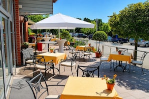 An outdoor patio with tables and chairs, a white umbrella, and potted plants. - Wolfsburg Sandkamp Hotel by Belvilla (Wolfsburg)