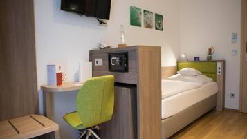 A compact hotel room with a bed, a desk, a chair, a TV mounted on the wall, and a small table.