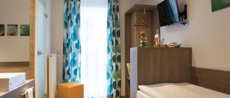 Quarto de hotel com cama, escrivaninha, cadeira, televisão e banheiro.