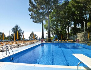 A swimming pool with a slide, surrounded by lounge chairs and tall trees. - Holiday Resort in Villanova D'albenga (Villanova d'Albenga)