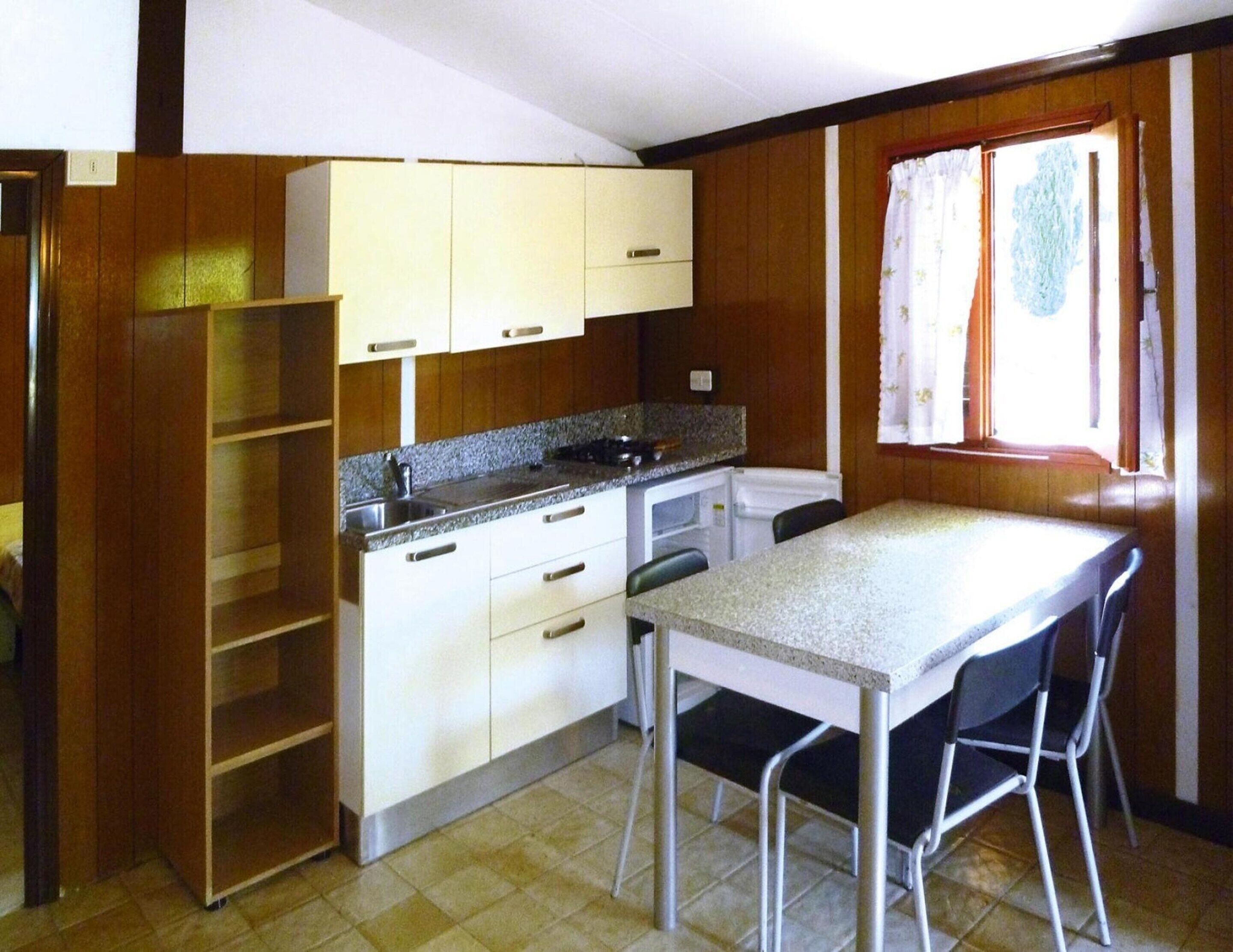 A compact kitchen with a dining area, wooden cabinets, a countertop, and a window with curtains.