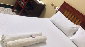 A hotel room with a neatly made bed, a wooden chair, a small desk, and a wall socket. - Cam Lodge (Tanga)