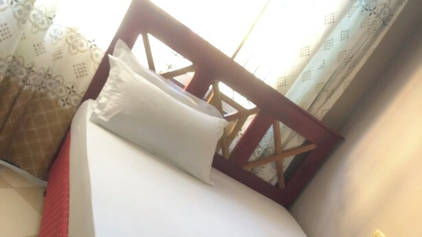 A single bed with a wooden headboard, white bedding, and a red skirted bed base. - Cam Lodge (Tanga)