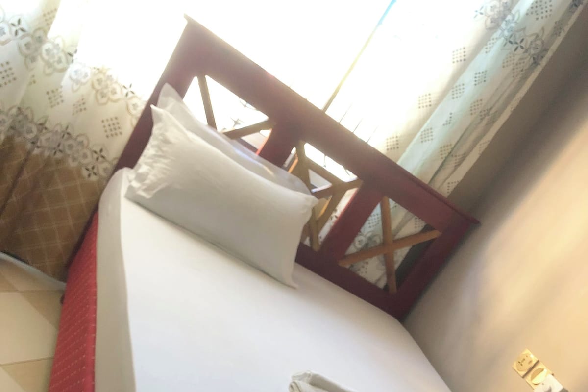 A single bed with a wooden headboard, white bedding, and a red skirted bed base.