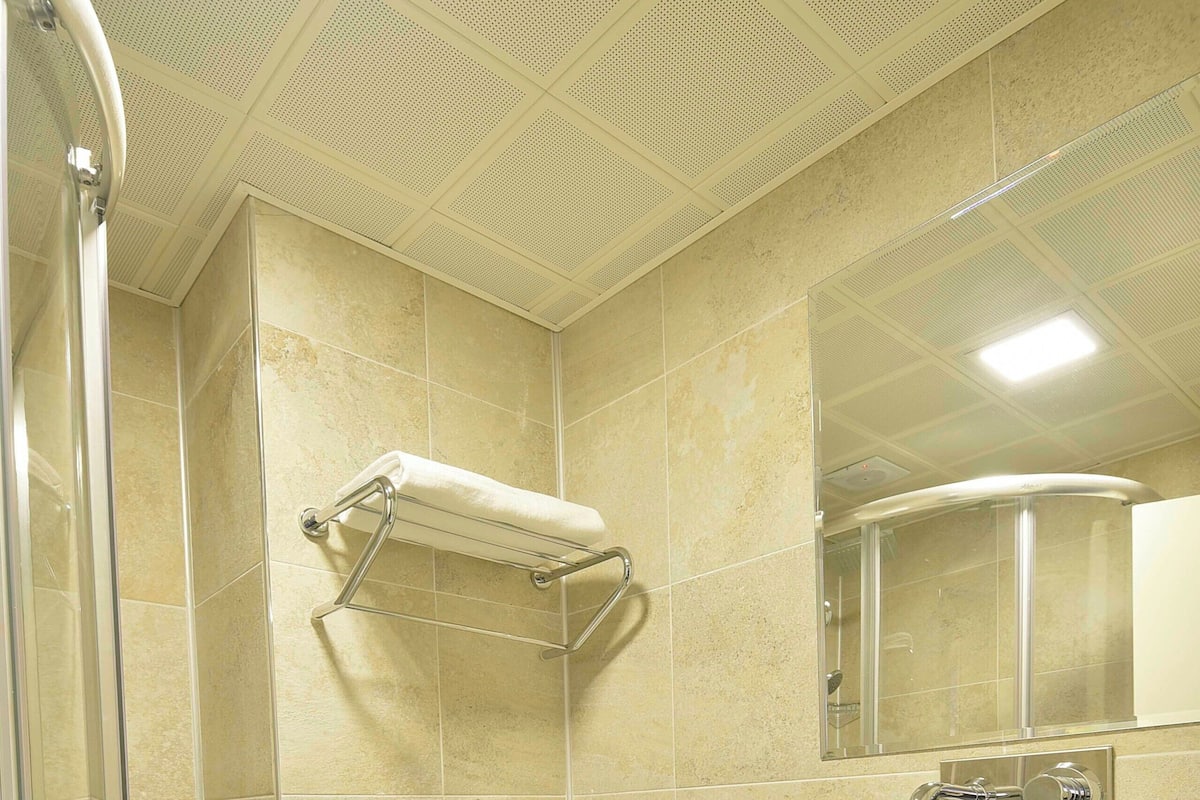 A bathroom with a glass shower enclosure, a white toilet, a sink with a mirror above it, and a towel rack.