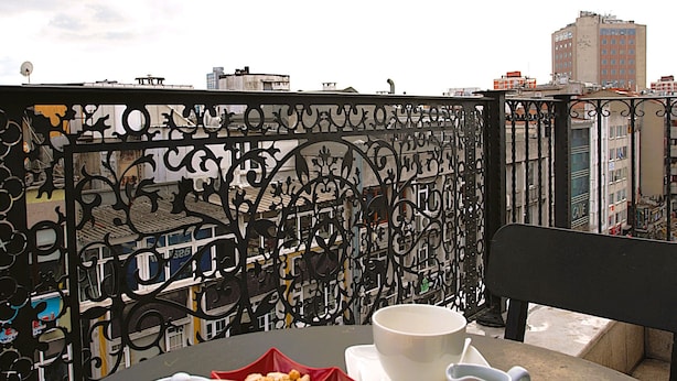 Ein Tisch mit Tasse und Schalen voller Snacks auf einem Balkon mit Metallgeländer und Stadtblick im Hintergrund.