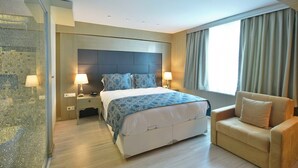 Ein modernes Hotelzimmer mit einem großen Bett, Nachttischlampen, einem Sofa und Blick ins Freie.
