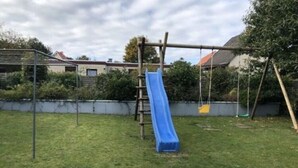 A playground with a blue slide, swings, and a climbing structure. - Strandnahe Ferienwohnung in Duhnen (Cuxhaven)