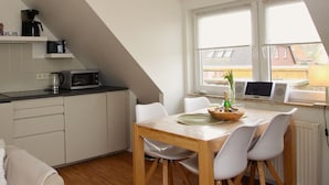 A modern kitchen with a dining area, white cabinets, a microwave, and a laptop on the windowsill. - Strandnahe Ferienwohnung in Duhnen (Cuxhaven)