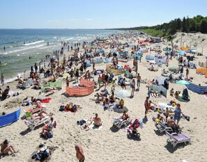 Uma praia cheia de gente, com vários guarda-sóis, espreguiçadeiras e pessoas aproveitando a costa.