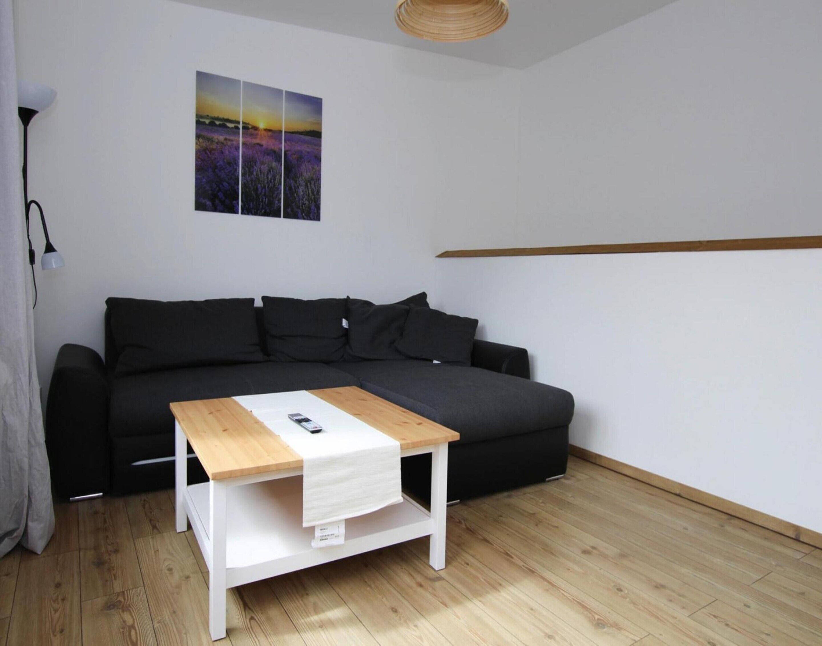 Un salon moderne avec un canapé gris foncé, une table basse en bois et un tableau représentant un paysage au coucher du soleil, accroché au mur.