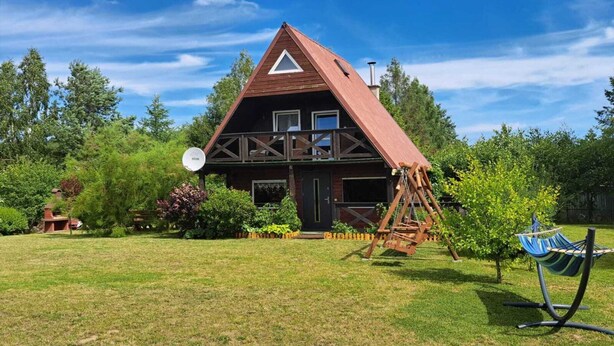 A wooden house with a triangular roof, a balcony, and a swing set in the yard. - Cottage in Koscierzyna With Lake Nearby (Koscierzyna)