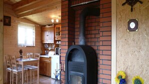 A cozy cabin interior with a wood-burning stove, wooden dining table, chairs, and a kitchen area. - Cottage in Koscierzyna With Lake Nearby (Koscierzyna)