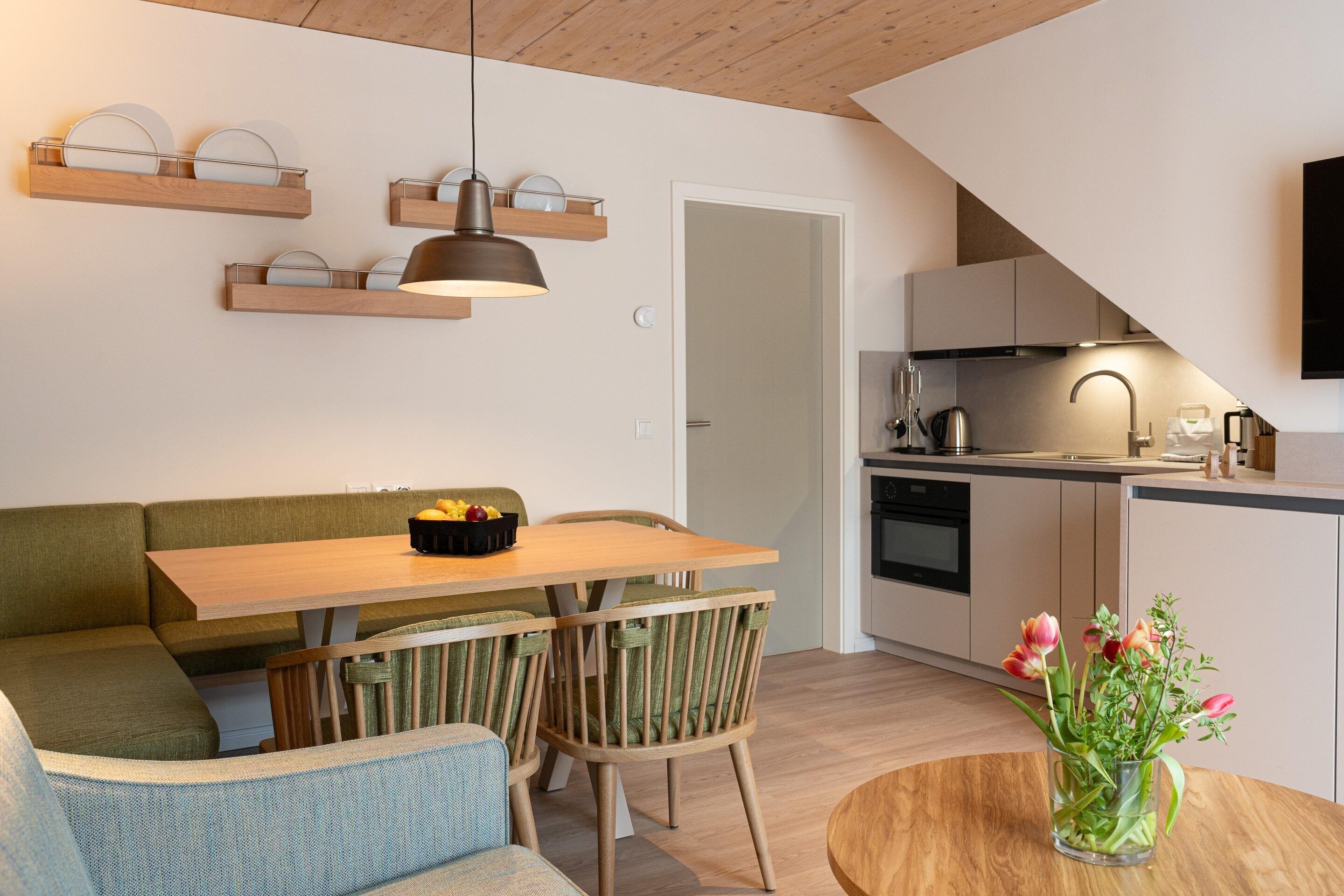 A modern kitchen with wooden cabinets, a dining area with a wooden table and chairs, and a built-in oven.