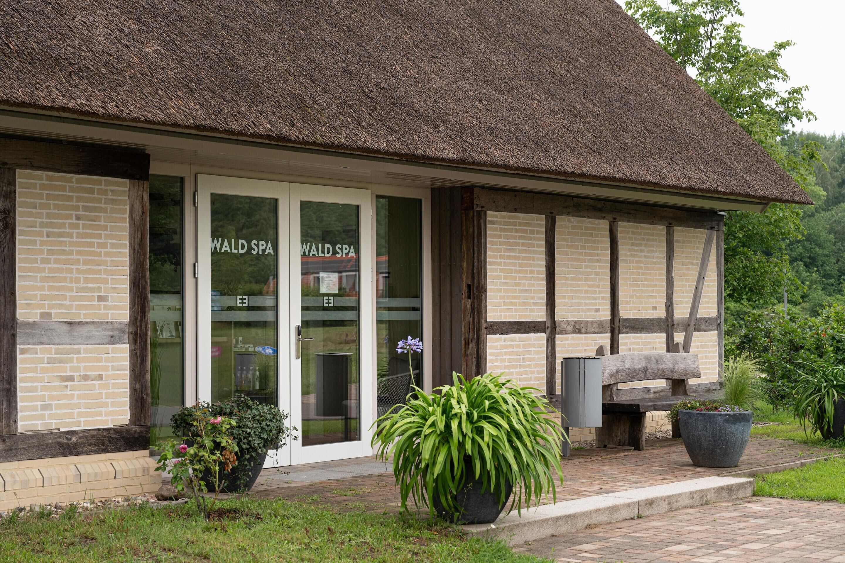 Un bâtiment abritant un centre de bien-être, doté d’un toit de chaume, de portes en verre et d’une façade en briques.