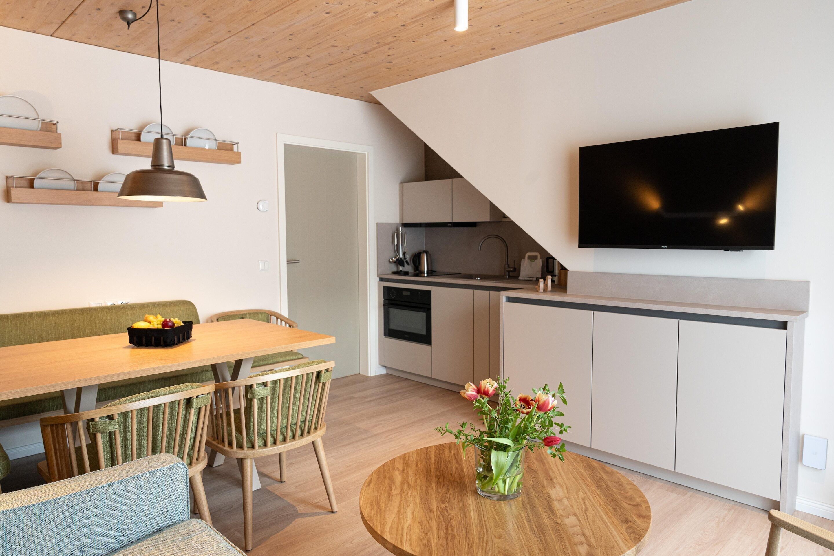 A modern kitchen with a flat-screen TV, wooden cabinets, and a dining area with a round table and chairs.