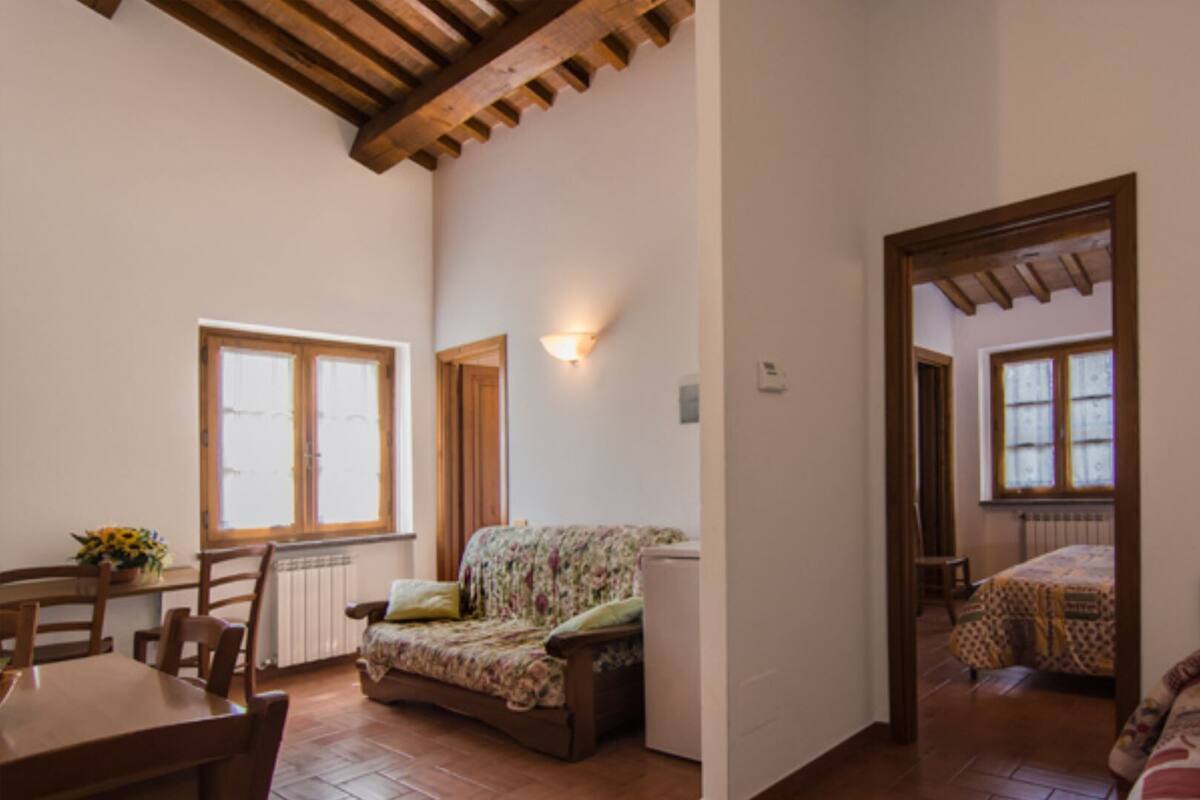 Una habitación acogedora con techo de madera, sofá floral, mesa de comedor con sillas y cama con colcha estampada.