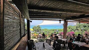 An outdoor dining area with tables and chairs, overlooking a scenic view of the sea and mountains.