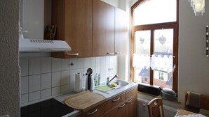 A kitchen with wooden cabinets, a stove, a sink, and a window with a view of buildings. - Wohnung in Ellefeld Nahe Skipisten (Ellefeld)