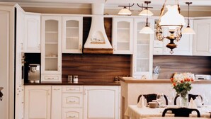 A kitchen with white cabinetry, a wooden backsplash, and a dining area with a table set for two.