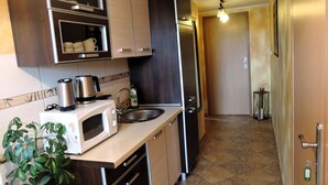 A compact kitchen with a microwave, kettle, and sink. There are cabinets and a plant.
