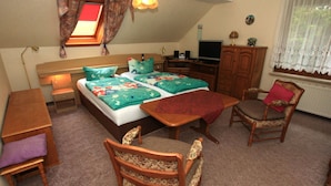 Een slaapkamer met een bed, een bureau, een stoel, een televisie en een raam met gordijnen.