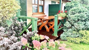 A wooden deck with a table and chairs, surrounded by lush greenery and flowering plants. - Comfortable Holiday Homes Close to the Beach (Mielno)