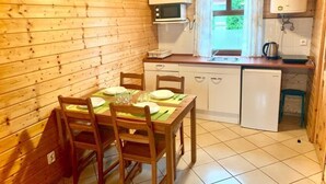 A compact kitchen with wooden walls, a dining table set for four, and basic amenities including a microwave, sink, and refrigerator. - Comfortable Holiday Homes Close to the Beach (Mielno)