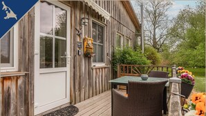 Une terrasse en bois avec une table et des chaises, une porte et un petit jardin agrémenté de fleurs.