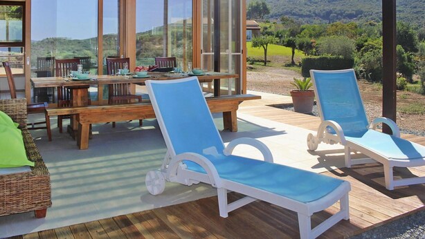 A covered outdoor dining area with a table and chairs, a wooden deck, and lounge chairs.