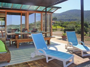 A covered outdoor dining area with a table and chairs, a wooden deck, and lounge chairs. - Holiday Home Magazzini With Sea View (Portoferraio)