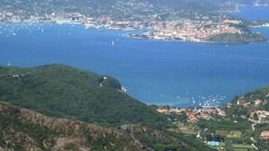 A coastal town with buildings along the waterfront, a marina with boats, and a hilly landscape in the background.