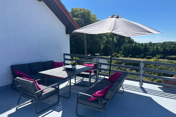 An outdoor seating area with a table, chairs, and a sofa, featuring a view of a forested landscape.