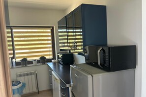 A compact kitchen with a microwave, a small refrigerator, and a window with blinds. - Apartment in Dabrowa Near the Sea (Swierzno)