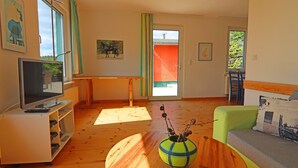 Een woonkamer met een televisie, een houten salontafel, een bank en een raam met gordijnen.