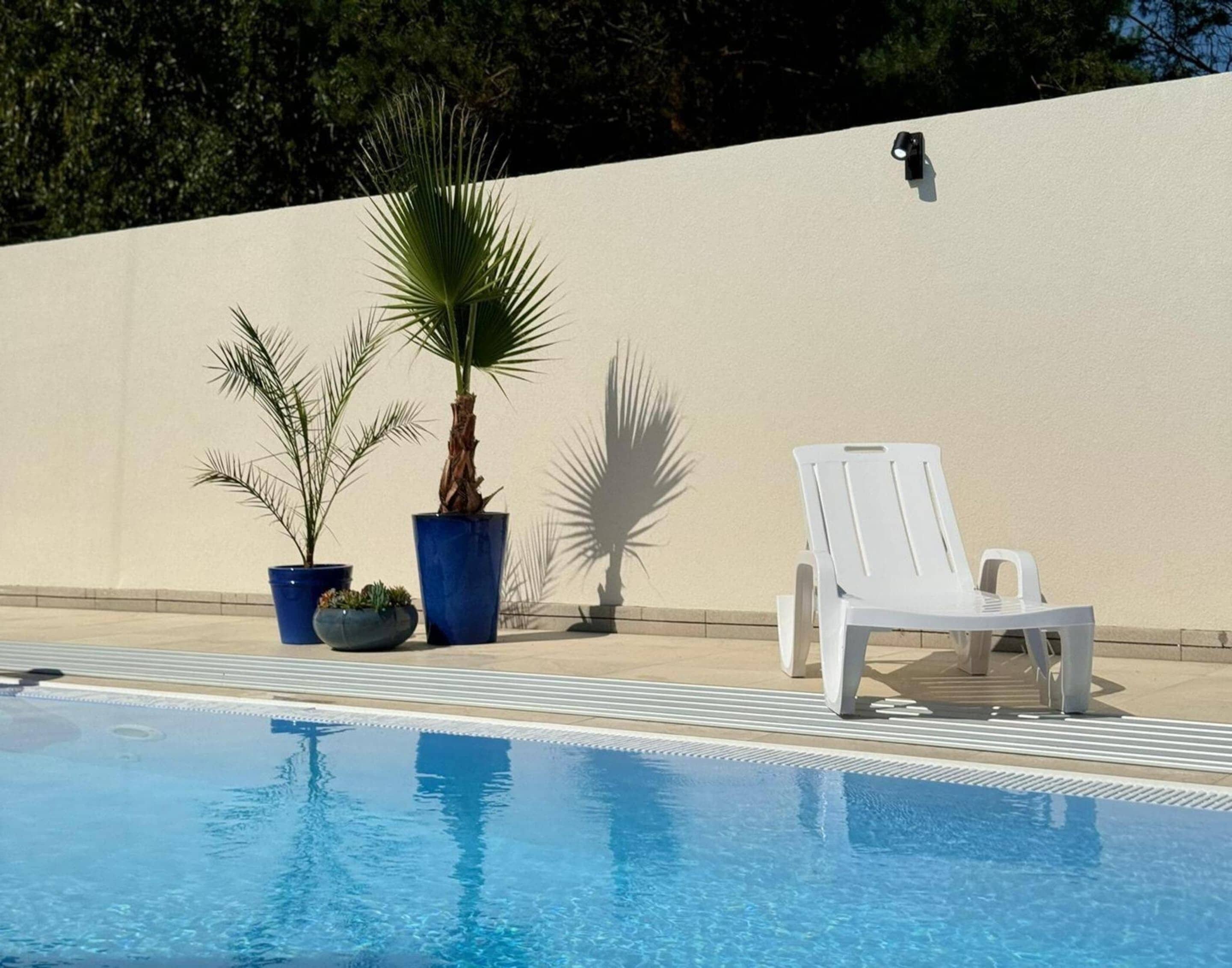 Une piscine avec des chaises longues et des plantes en pot.