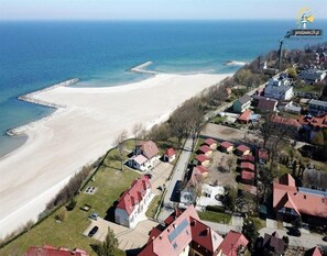 An aerial view of a coastal area with a sandy beach, residential buildings, and a pier extending into the sea. - Apartment in Jaroslawiec Near Seaside Beach (Postomino)