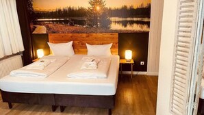 A double bed with a wooden headboard, two bedside tables with lamps, and a large scenic wall mural.