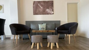 A modern living room with a grey sofa, two black armchairs, a wooden coffee table, and two grey ottomans.