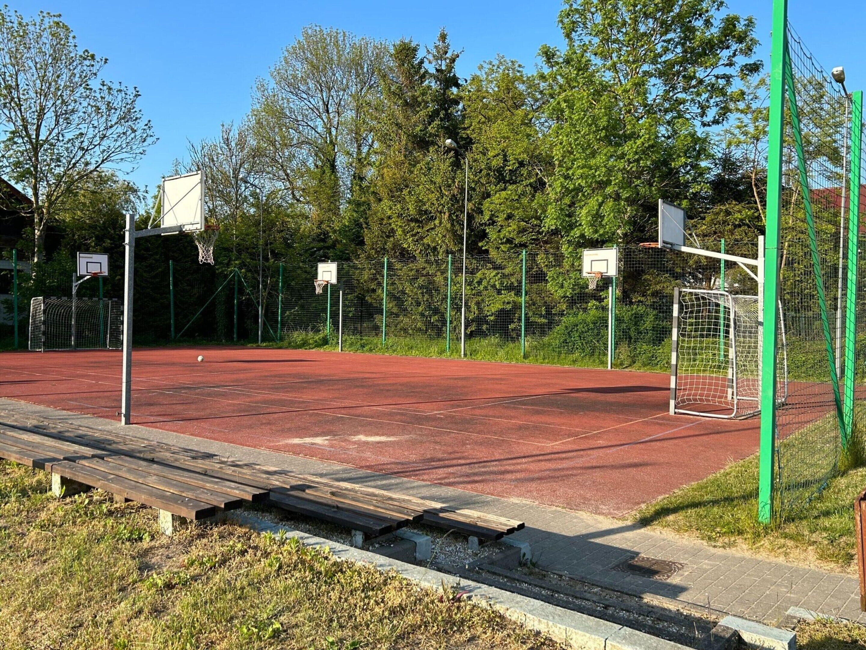 Una cancha de baloncesto al aire libre con varias canastas, rodeada por una cerca verde y árboles.